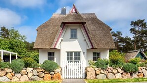 Een wit huis met rieten dak, een stenen muur en een witte hekwerk.