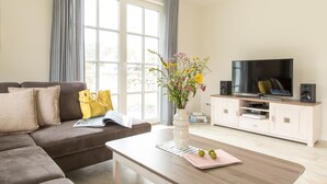 Een moderne woonkamer met een bank, salontafel, televisie en een raam met gordijnen.