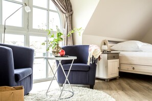 A bedroom with a bed, a nightstand, a table with a lamp, and two armchairs.
