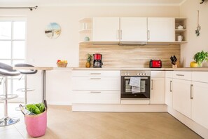 Una cocina moderna con armarios blancos, horno empotrado y cafetera.