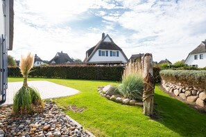 A well-maintained garden with a paved walkway, a stone wall, and a thatched-roof house.