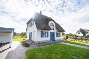 A two-story house with a thatched roof, white walls, and blue shutters.