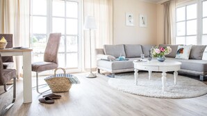 Ein modernes Wohnzimmer mit grauem Sofa, einem runden Couchtisch und einem Essbereich mit Tisch und Stühlen.