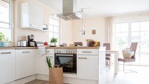 Eine moderne Küche mit weißen Schränken, einem eingebauten Backofen und einer Kaffeemaschine. Ein Fenster sorgt für natürliches Licht und bietet einen Blick auf die Stadt.