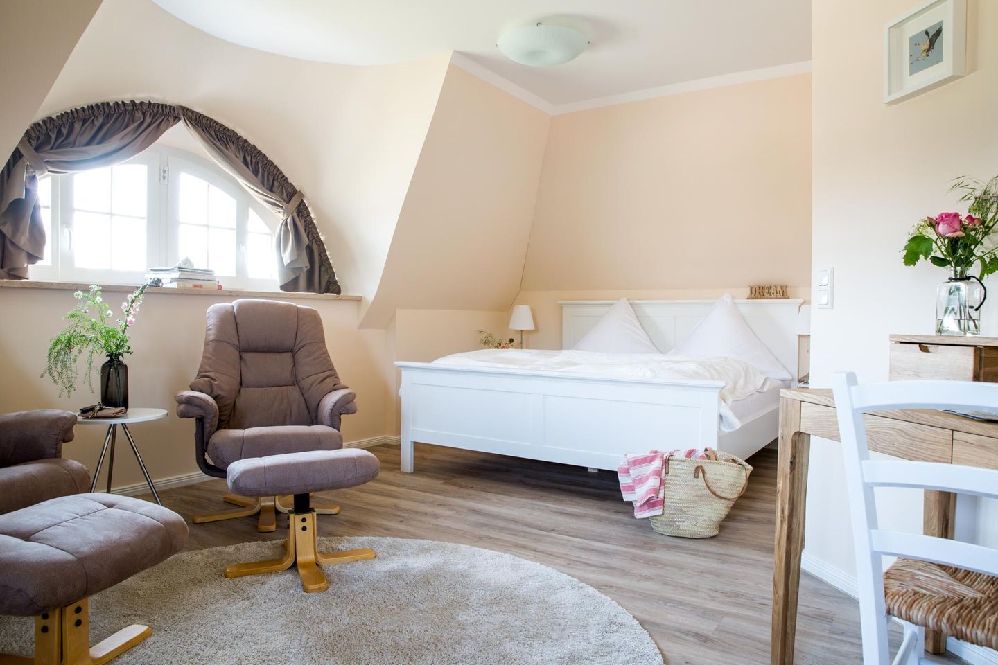 A bedroom with a bed, a chair, a small table, and a window with curtains.