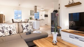 Una sala de estar moderna con sofá, mesa de centro y televisor. Se ve una cocina al fondo con estufa y microondas.