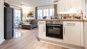 Una cocina moderna con horno integrado, un comedor con sofá y vistas a la ciudad a través de amplios ventanales.