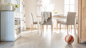 Un comedor con una mesa, sillas, un mueble con cajones y una pelota de baloncesto en el suelo.
