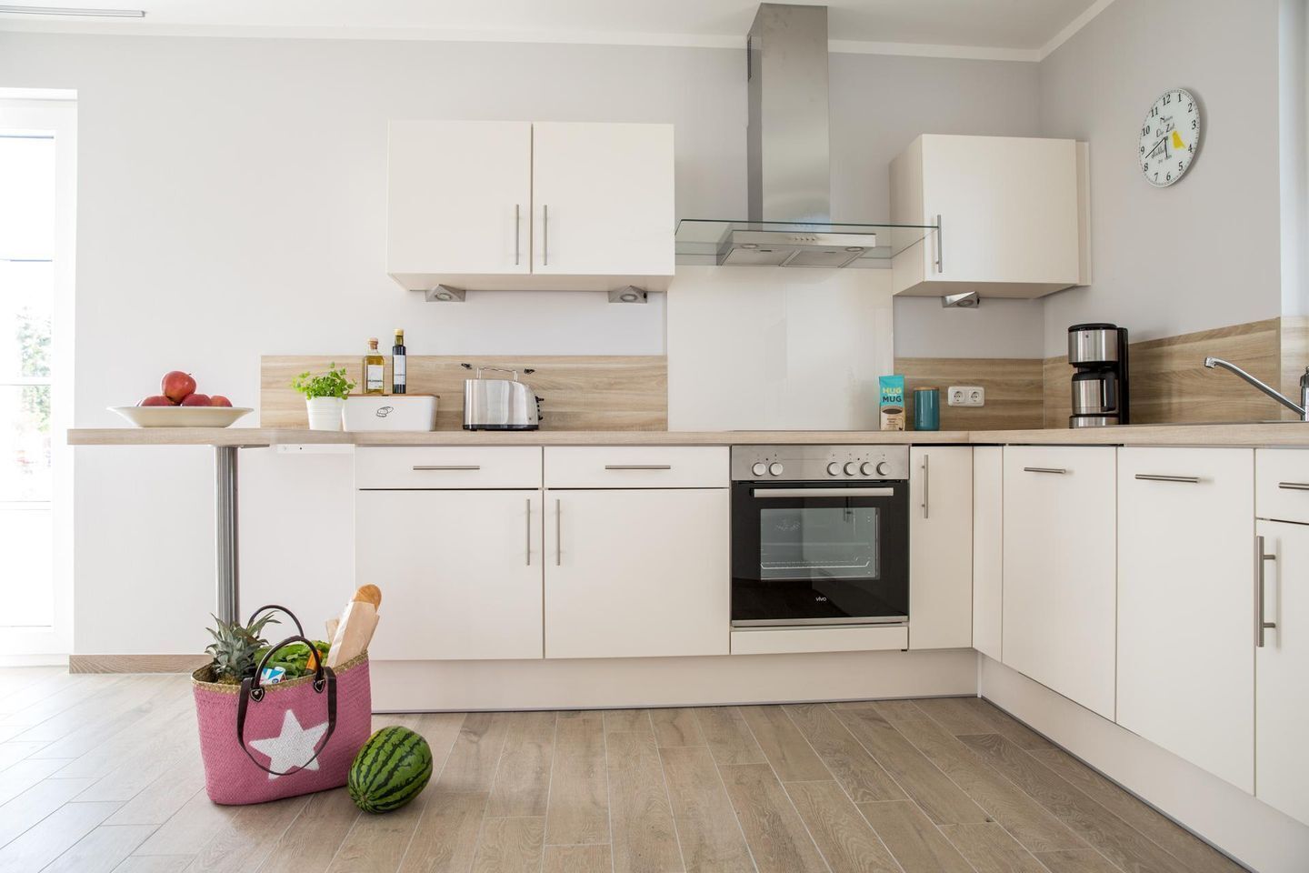 A modern kitchen with white cabinets, a built-in oven, and a stainless steel range hood.