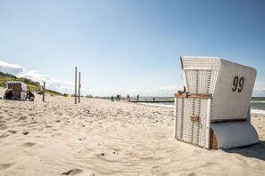 Ein Strand mit einem Korbstuhl, der mit '99' gekennzeichnet ist, und einer Holzkonstruktion im Sand.