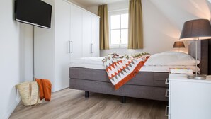 Un dormitorio moderno con cama, mesita de noche, lámpara, armario y televisor en la pared.