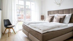 A bedroom with a bed, a chair, a lamp, and a deer skull on the wall.