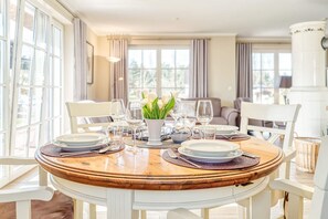 A dining area with a round wooden table set for four, surrounded by white chairs. - Vacation home Haubenlerche 20 - Holiday home Haubenlerche 20 - Close to nature (Fuhlendorf)