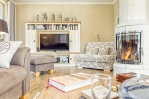 A cozy living room with a fireplace, a television, and a bookshelf filled with books. - Haubenlerche 20 Vacation Home - Haubenlerche 20 Vacation Home - Close to Nature (Fuhlendorf)