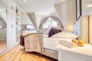 Ein Schlafzimmer mit einem Bett, einem Nachttisch mit Büchern und Äpfeln, einem Kleiderschrank und einem Fernseher auf einer Kommode.