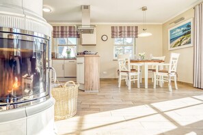A modern kitchen with a built-in stove, a dining area with white chairs, and a large window. - Haubenlerche 20 Vacation Home - Haubenlerche 20 Vacation Home - Close to Nature (Fuhlendorf)