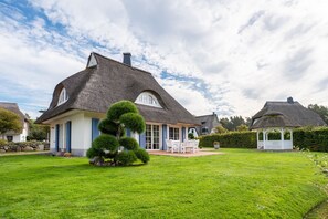Une maison avec un toit de chaume, une pelouse bien entretenue et un petit kiosque.