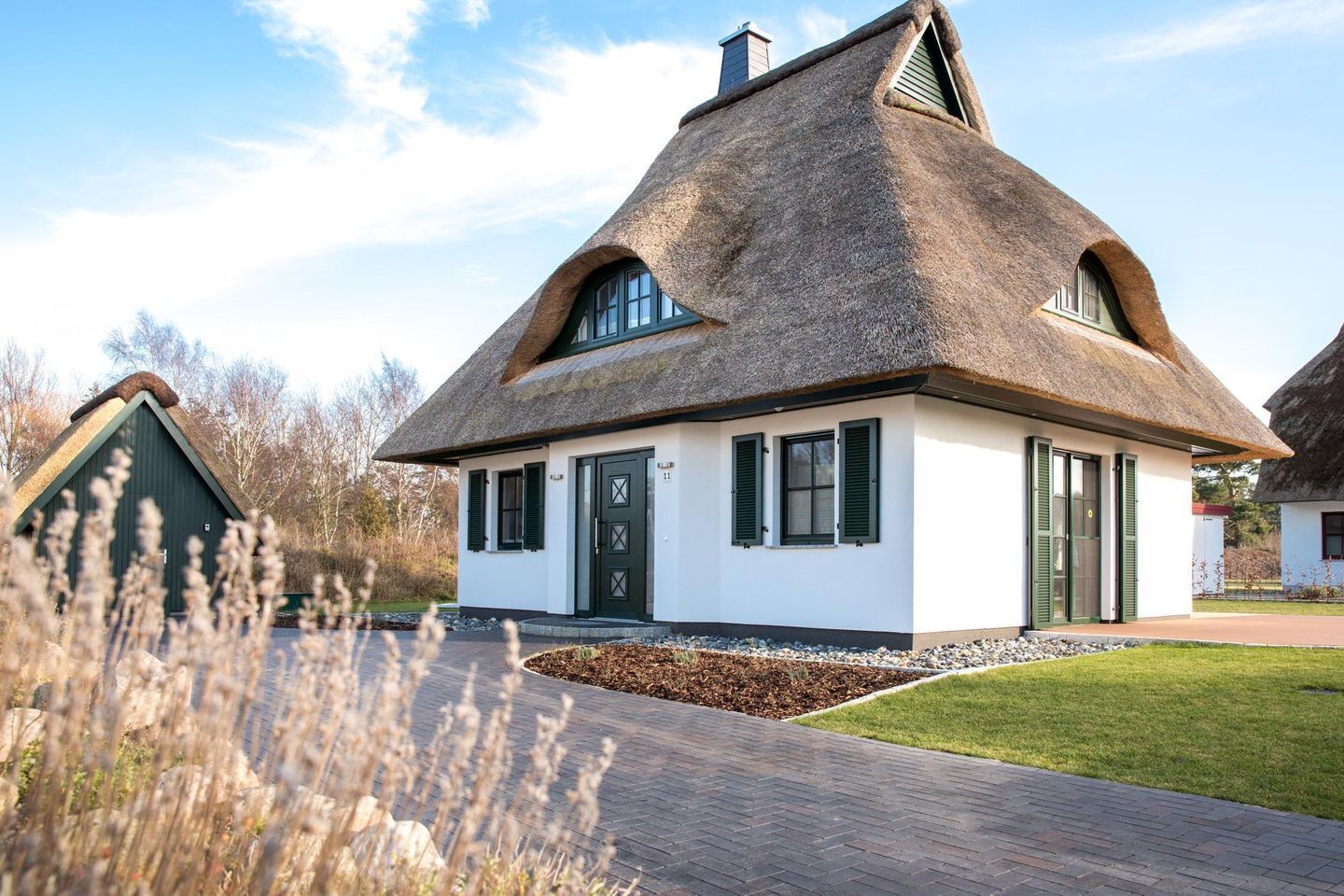 A traditional thatched-roof house with a white exterior, a green door, and a small front garden.