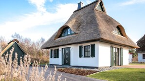 A traditional thatched-roof house with a white exterior, a green door, and a small front garden.