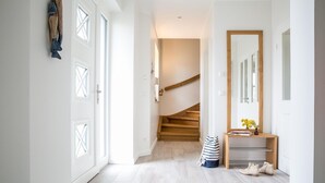 A hallway with a wooden staircase, a mirror, and a small wooden console table with books and flowers.