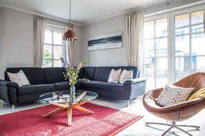Una sala de estar moderna con un sofá gris oscuro, una mesa de centro de vidrio, una alfombra roja y un sillón de cuero marrón.