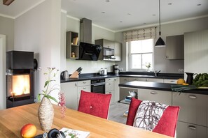 Una cocina moderna con estufa integrada, un comedor con mesa de madera y vistas al salón.