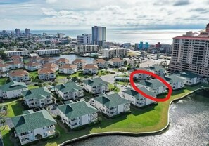 Un área residencial costera con varias casas de dos pisos, un puerto deportivo y el horizonte de una ciudad al fondo.