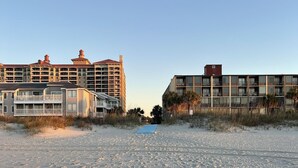 Un hôtel situé en bord de mer, doté de nombreux balcons, d’une plage de sable fin et offrant une vue sur un ciel dégagé.