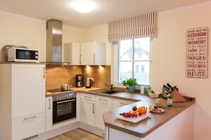 A modern kitchen with white cabinets, a microwave, a coffee maker, and a window with a view of a house.