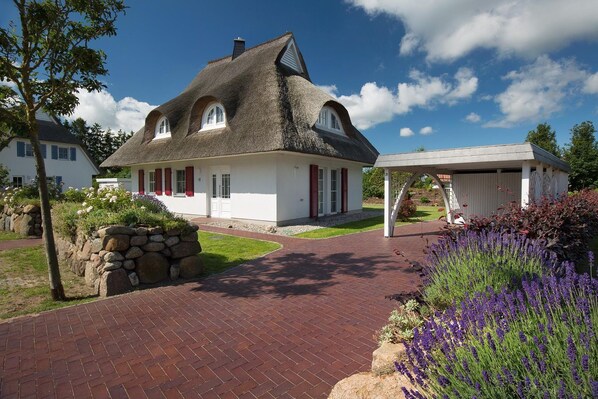 A house with a thatched roof, white walls, and red shutters.