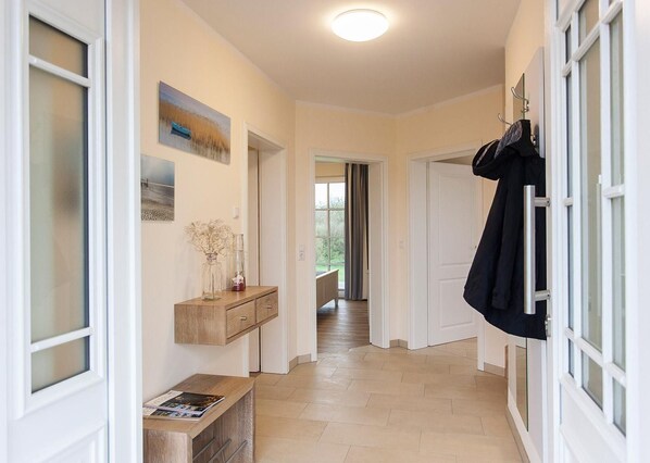 A hallway with a wooden console table, a vase with dried flowers, and a coat hanging on a rack.