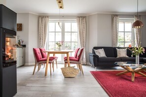 A modern living room with a fireplace, a dining table with chairs, a sofa, and a coffee table. - Vacation home Seeadler 7 - Holiday home Seeadler 7 - Close to nature (Fuhlendorf)