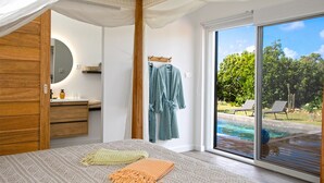A bedroom with a large bed, a bathroom with a mirror, and a view of a swimming pool.