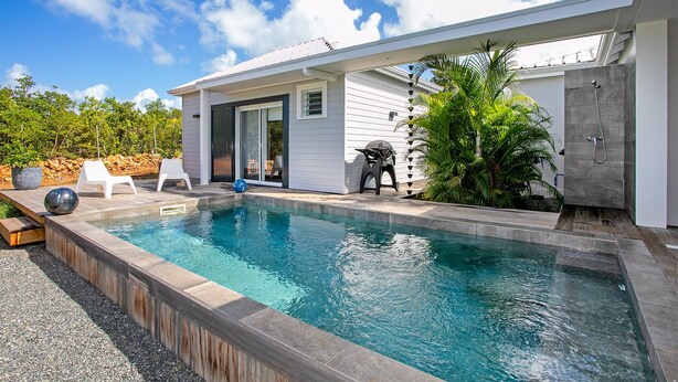 A modern outdoor swimming pool area with a clear blue pool, a covered patio, and a sliding glass door leading to a private outdoor space.
