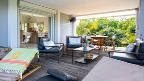 A modern outdoor living area with a wooden deck, furnished with a sofa, chairs, and a dining table.