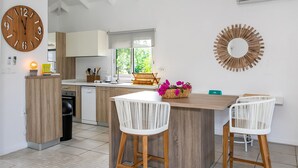 A modern kitchen with wooden cabinets, a large round clock, a dining area with two white wicker chairs, and a decorative mirror on the wall.