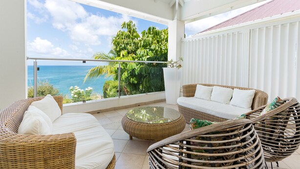 A balcony with wicker furniture, a glass coffee table, and a view of the ocean. - Blue Sailing | Ocean View - Located in  Wonderful Happy Bay with Private Pool (Saint Martin)