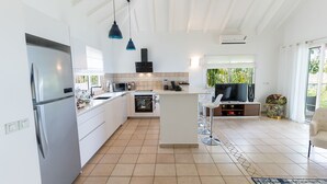 A modern kitchen with white cabinetry, a built-in oven, and a large island with bar stools. - Blue Sailing | Ocean View - Located in  Wonderful Happy Bay with Private Pool (Saint Martin)