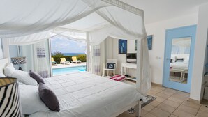 A bedroom with a bed, a TV, and a view of a pool and chairs. - Blue Sailing | Ocean View - Located in  Wonderful Happy Bay with Private Pool (Saint Martin)