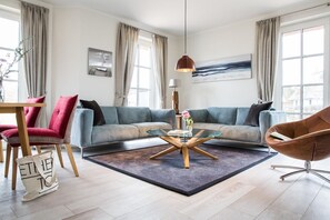 En moderne stue med en modulsofa, et glasbord, en rød lænestol, en brun læderstol og et stort vindue med gardiner.