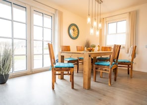 Un comedor con mesa y sillas de madera, un reloj en la pared y ventanas grandes.
