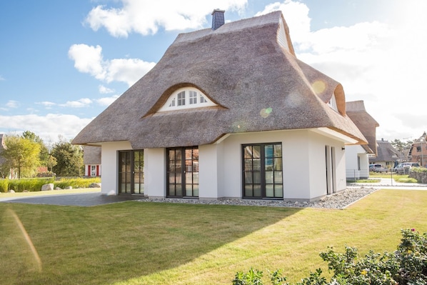 A thatched-roof house with a white exterior, large windows, and a well-maintained lawn.