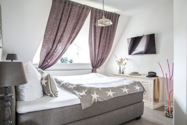 Un dormitorio moderno con cama, mesita de noche, lámpara y televisor en la pared.