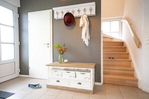Ein Flur mit einer Holztreppe, einem weißen Konsolentisch mit Schubladen, einer Blumenvase und einem Kleiderhaken mit Hut und Kleidungsstück.
