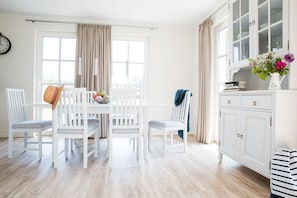 Um quarto claro com uma mesa de jantar branca, cadeiras e um armário com gavetas.