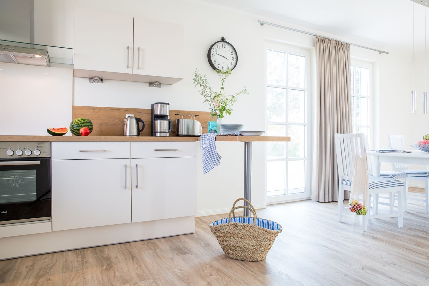 A modern kitchen with white cabinets, a built-in oven, a coffee maker, and a clock on the wall.