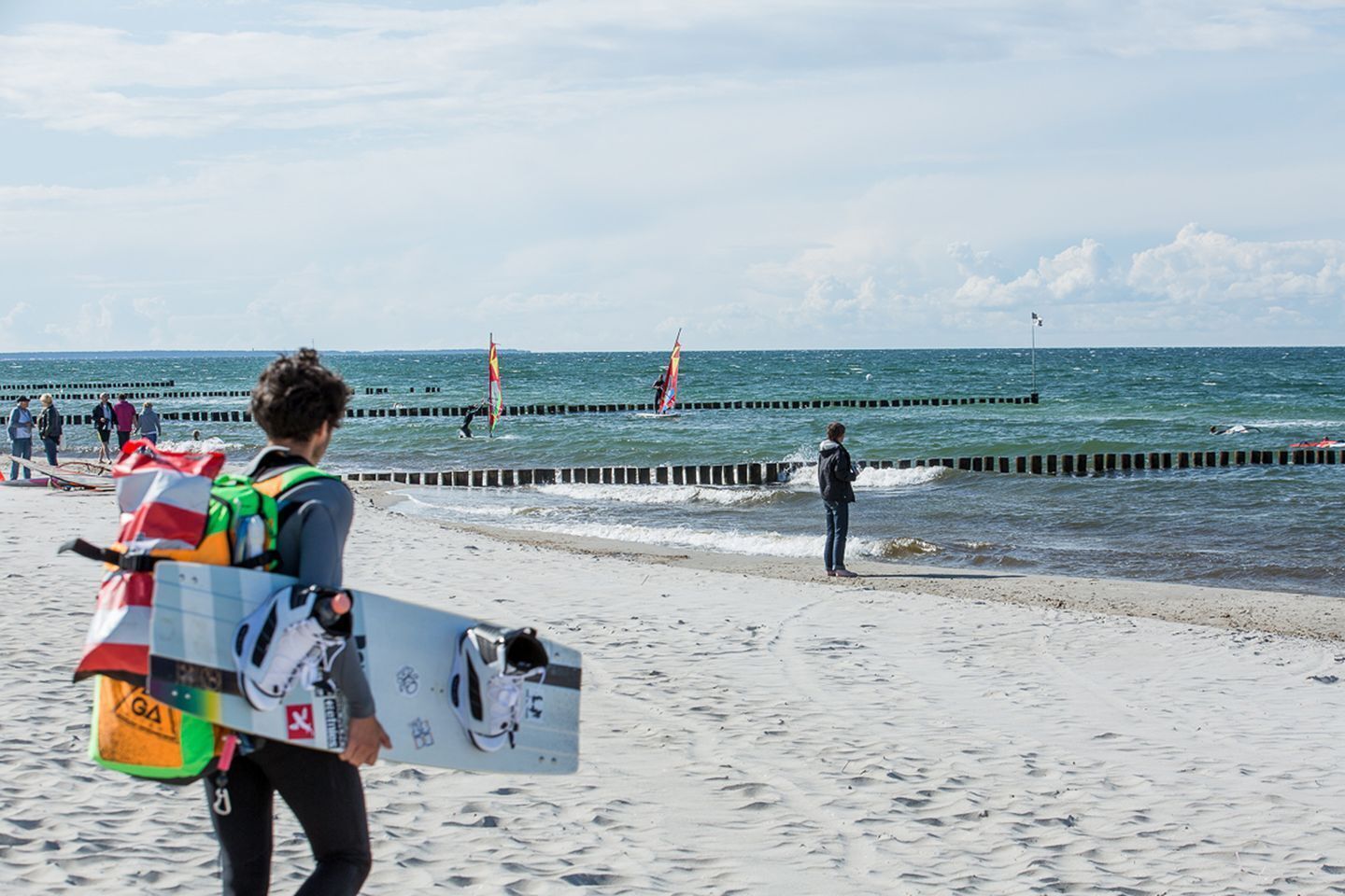 A beach with a person carrying a surfboard and a life jacket.