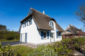 A house with a steeply pitched roof, white exterior walls, and blue shutters.