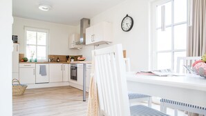 A bright kitchen with white cabinets, a stainless steel range hood, and a dining area with a white table and striped chairs.