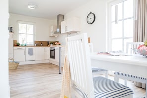 A bright kitchen with white cabinets, a stainless steel range hood, and a dining area with a white table and striped chairs.